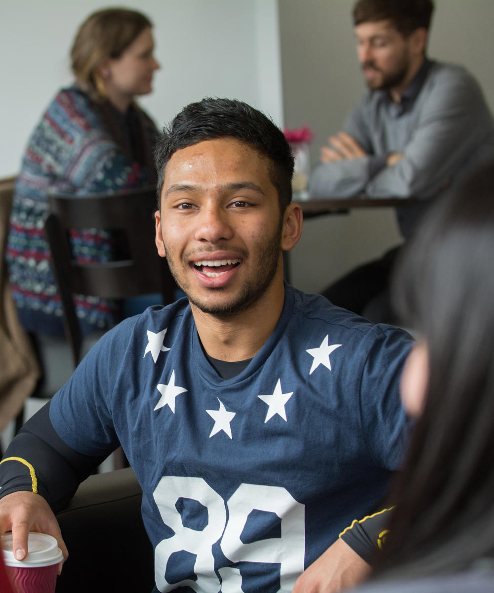 Imager of international student sat with a group of people at a table in the lounge 
