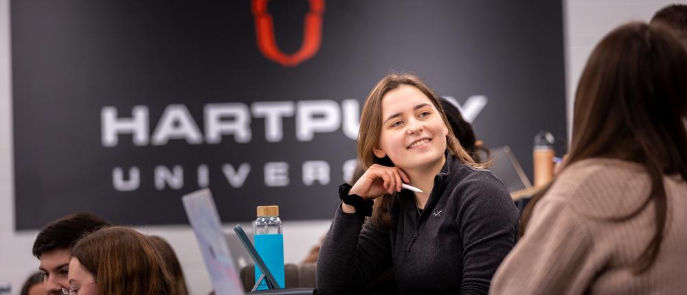 Image of students sat in a lecture theatre with a student smiling at other nearby students