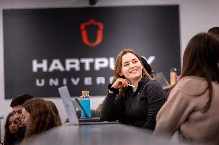 Image of students sat in a lecture theatre with a student smiling at other nearby students