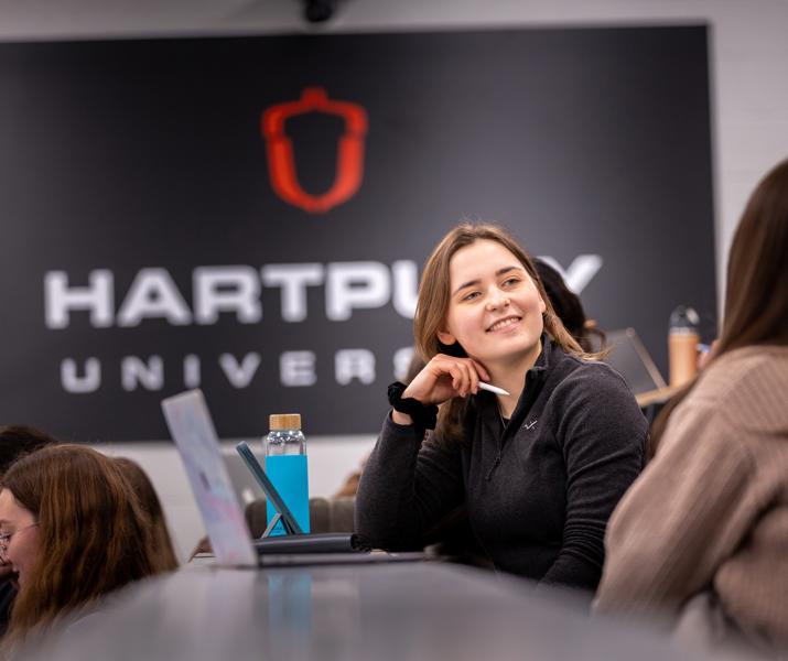 Image of students sat in a lecture theatre with a student smiling at other nearby students