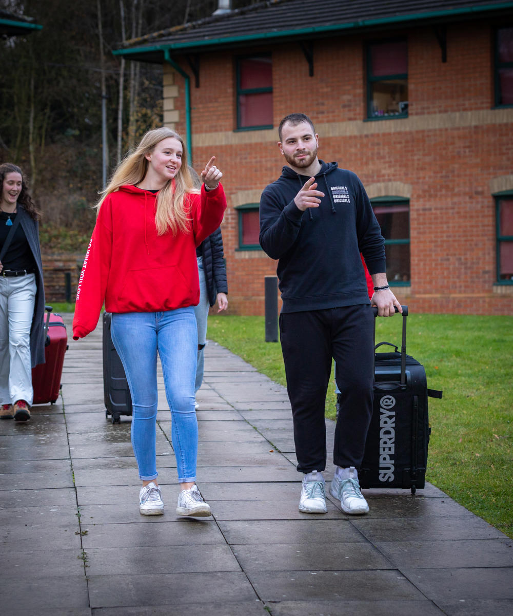 Image of a group of students walking on campus with their luggage on moving in day