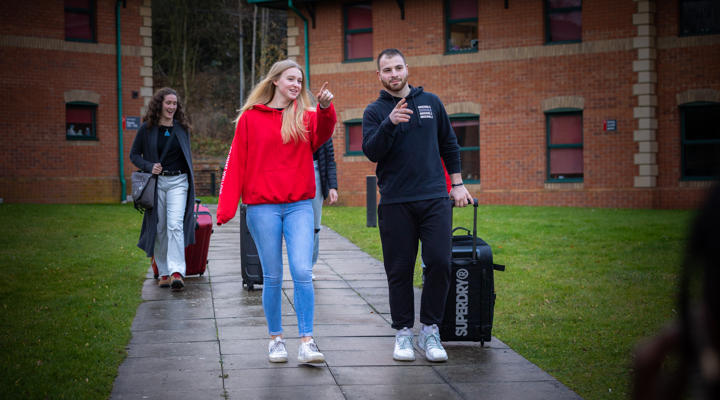 Image of a group of students walking on campus with their luggage on moving in day