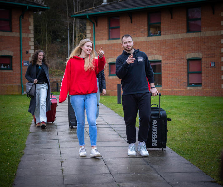 Image of a group of students walking on campus with their luggage on moving in day
