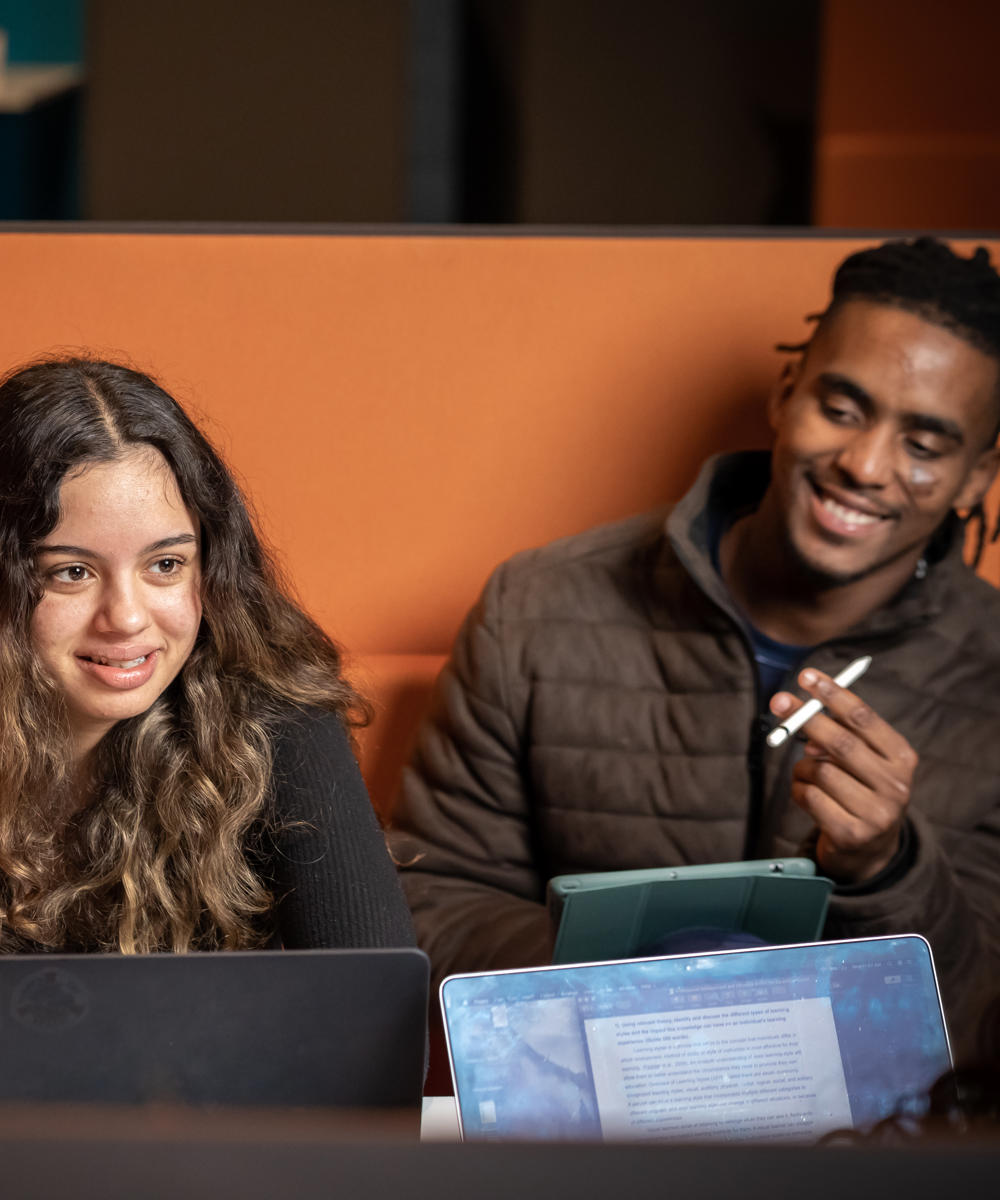 Image of a group of international students sat at a table talking with their laptops