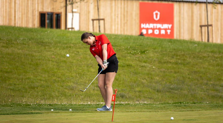 Female Student Practising In Short Game Golf Area