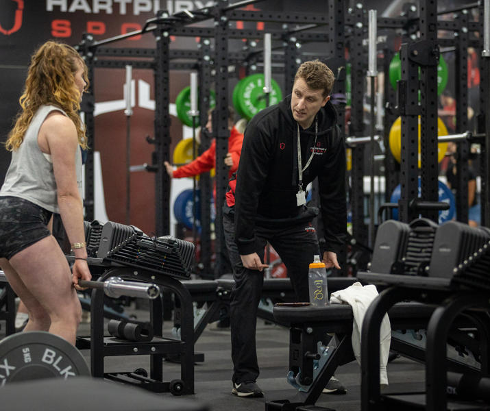 Women lifting bar in gym while man gives instructions